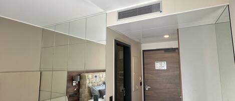 A modern hotel room with a sofa, a wooden floor, a mirror, and a door.