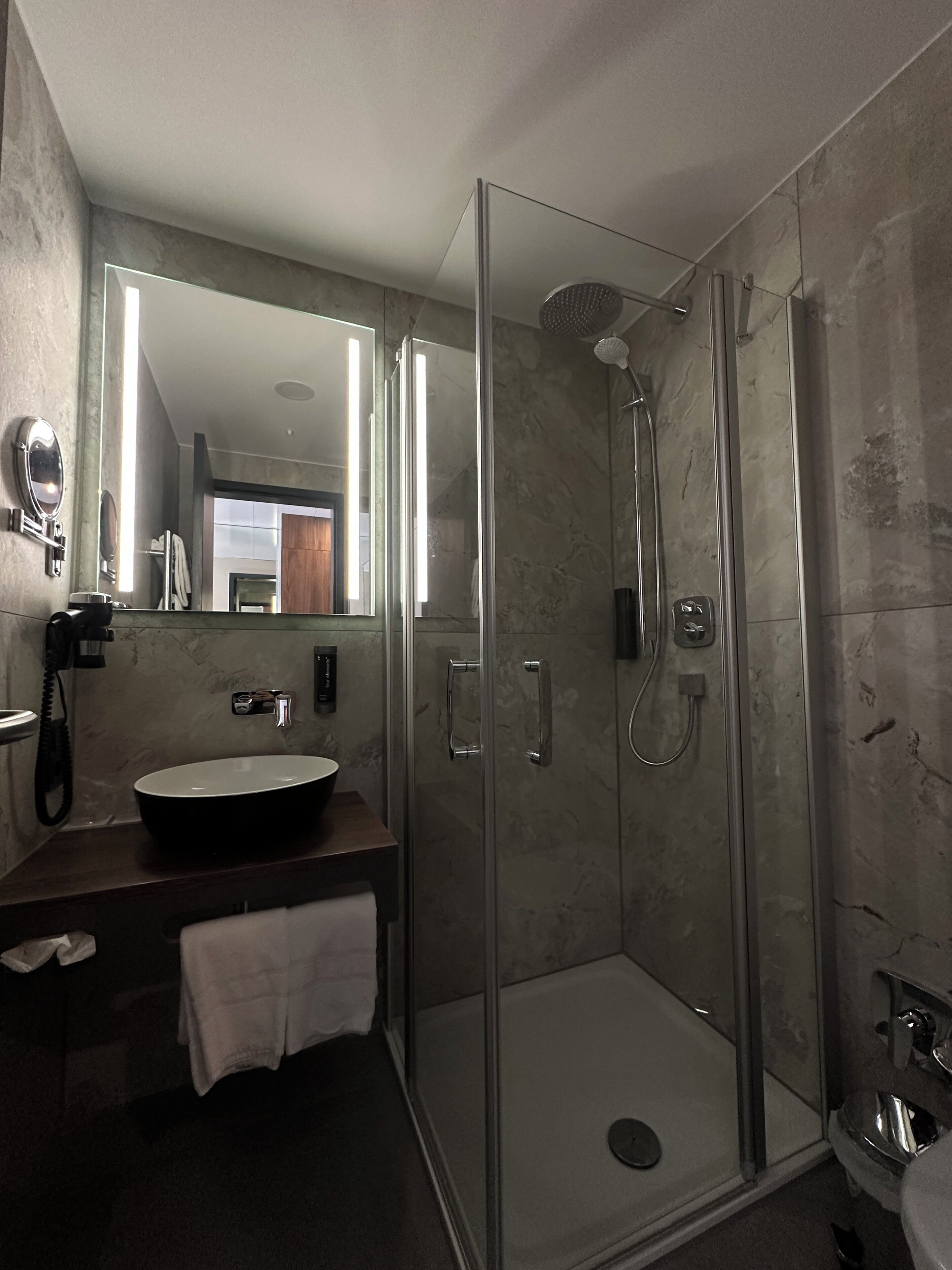 A modern bathroom with a glass-enclosed shower, a sink with a mirror, and a telephone.
