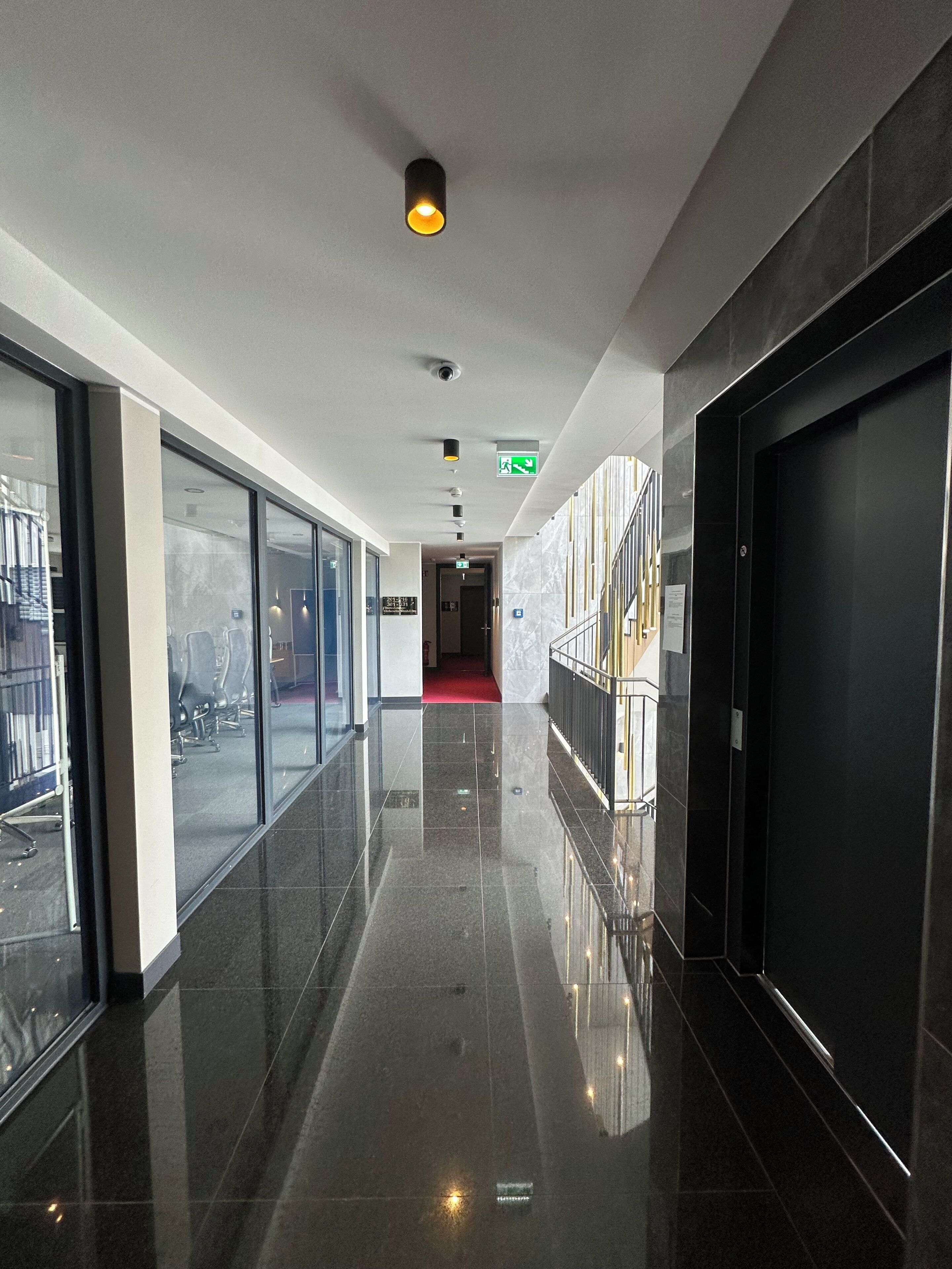 Un pasillo moderno de hotel con puertas de vidrio, una alfombra roja y un ascensor negro.