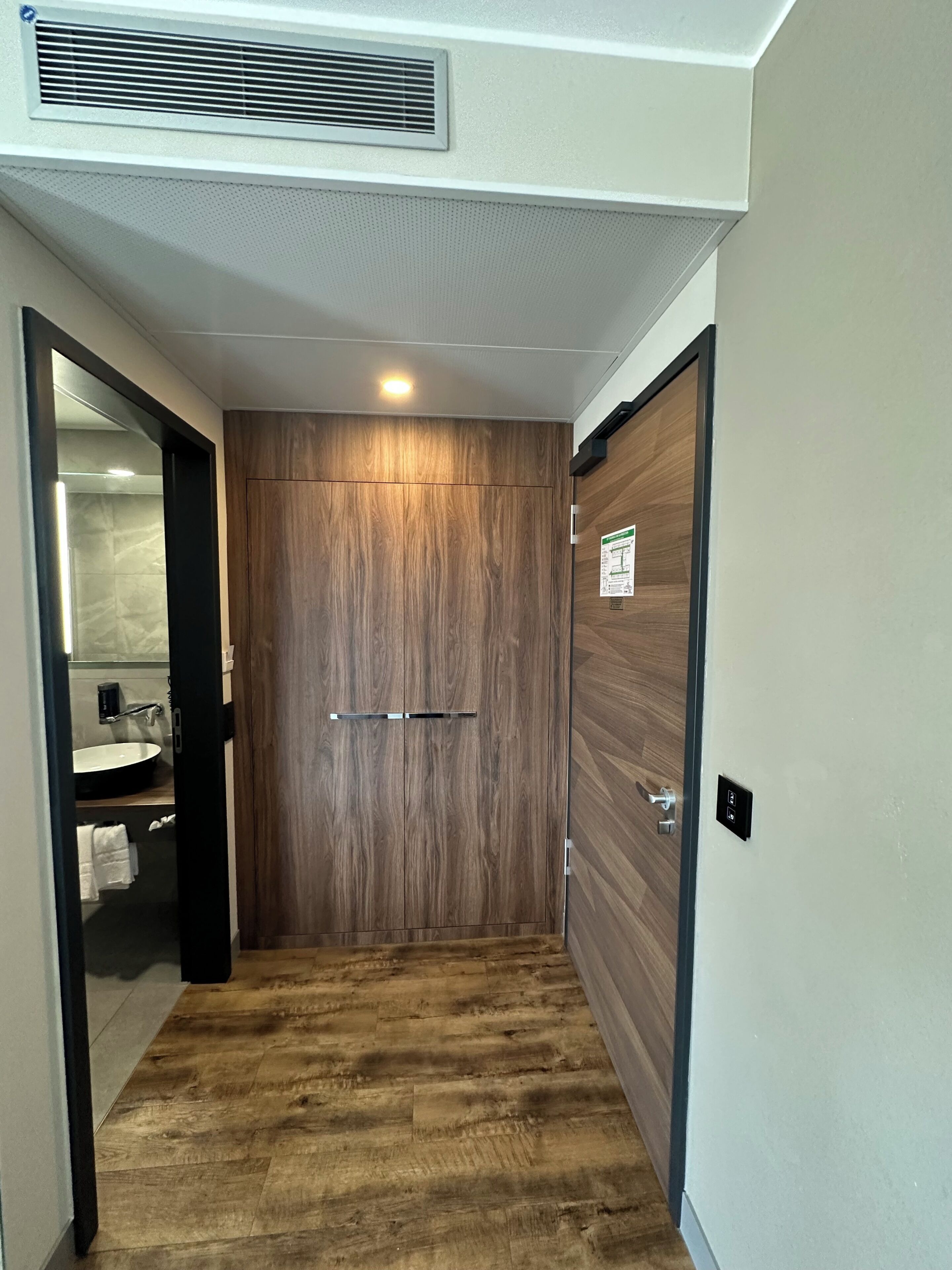 Un corridoio con una porta in legno, una bocchetta d'aerazione e un pavimento piastrellato.