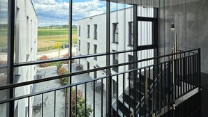 Et moderne interiør med store vinduer, en trappe og udsigt til bygninger og grønne områder udenfor.