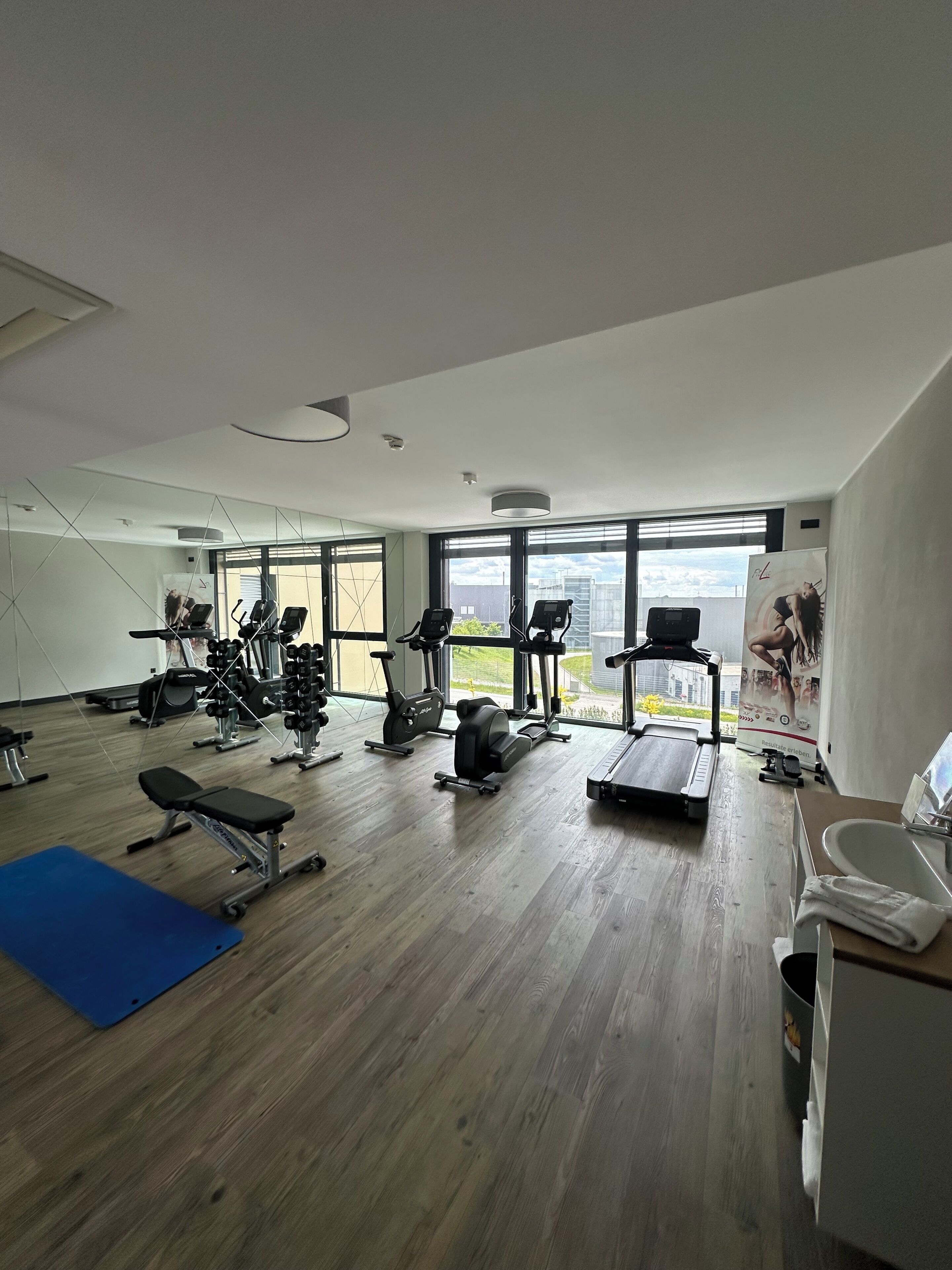 Une salle de sport équipée de matériel d’exercice, dotée de grandes fenêtres et d’un tapis bleu.