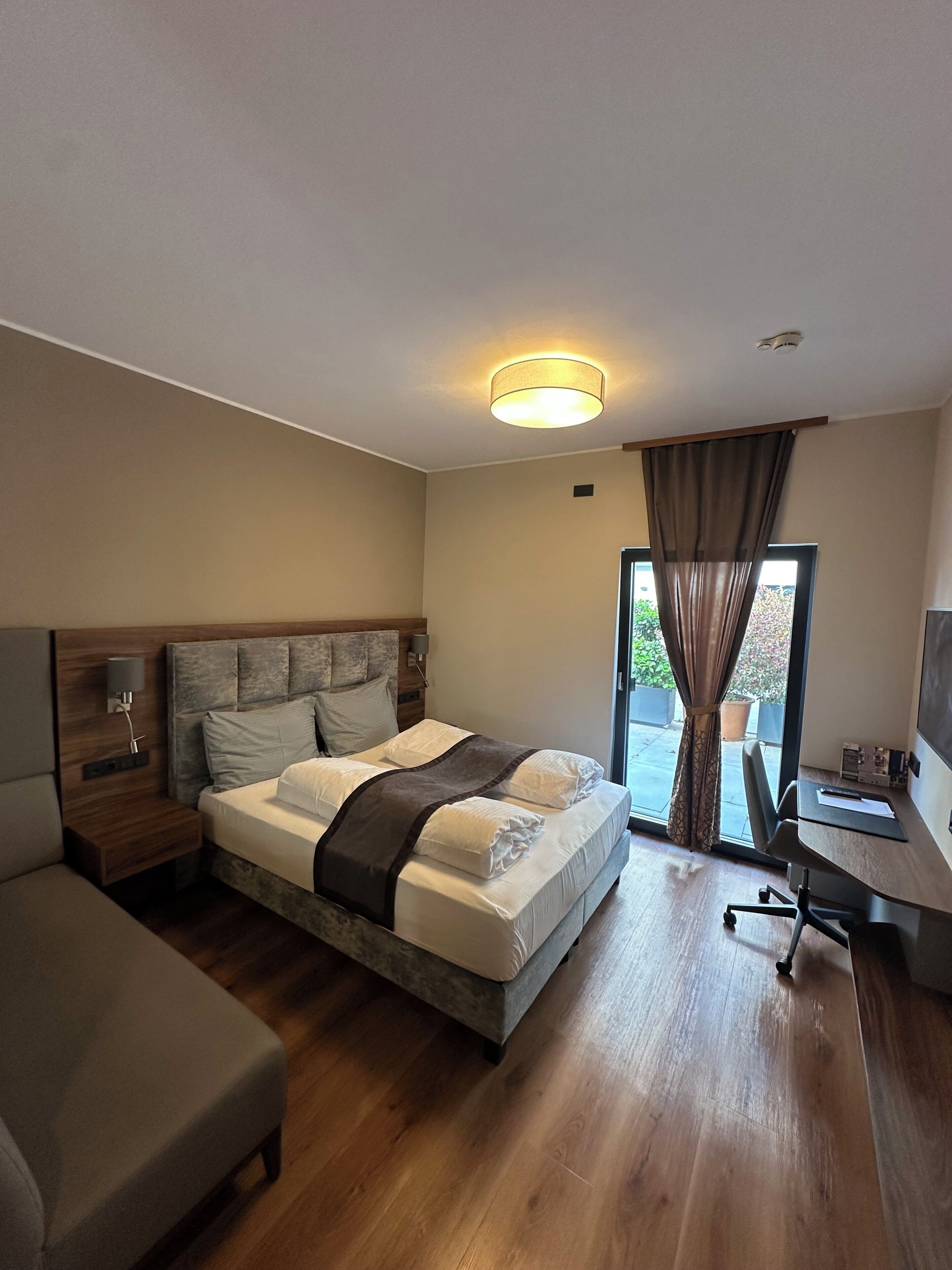 Een moderne hotelkamer met een bed, een bureau, een stoel, een nachtkastje en uitzicht op de omgeving.