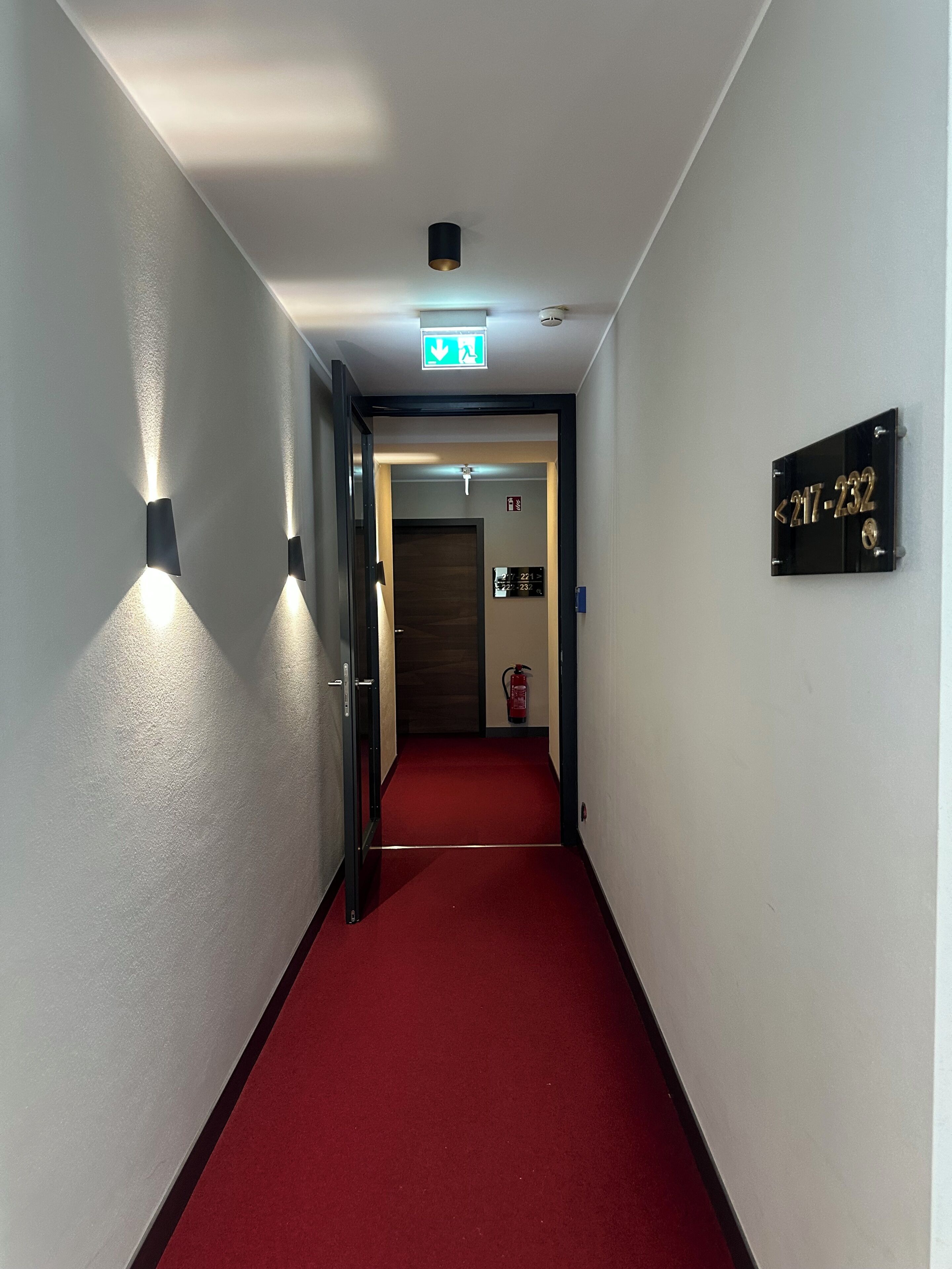 A hallway with a red carpet, a door at the end, and a sign with numbers.