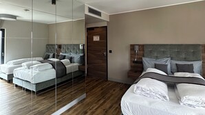 Et moderne hotelværelse med et stort spejl, to senge, trægulv og en synlig dør.