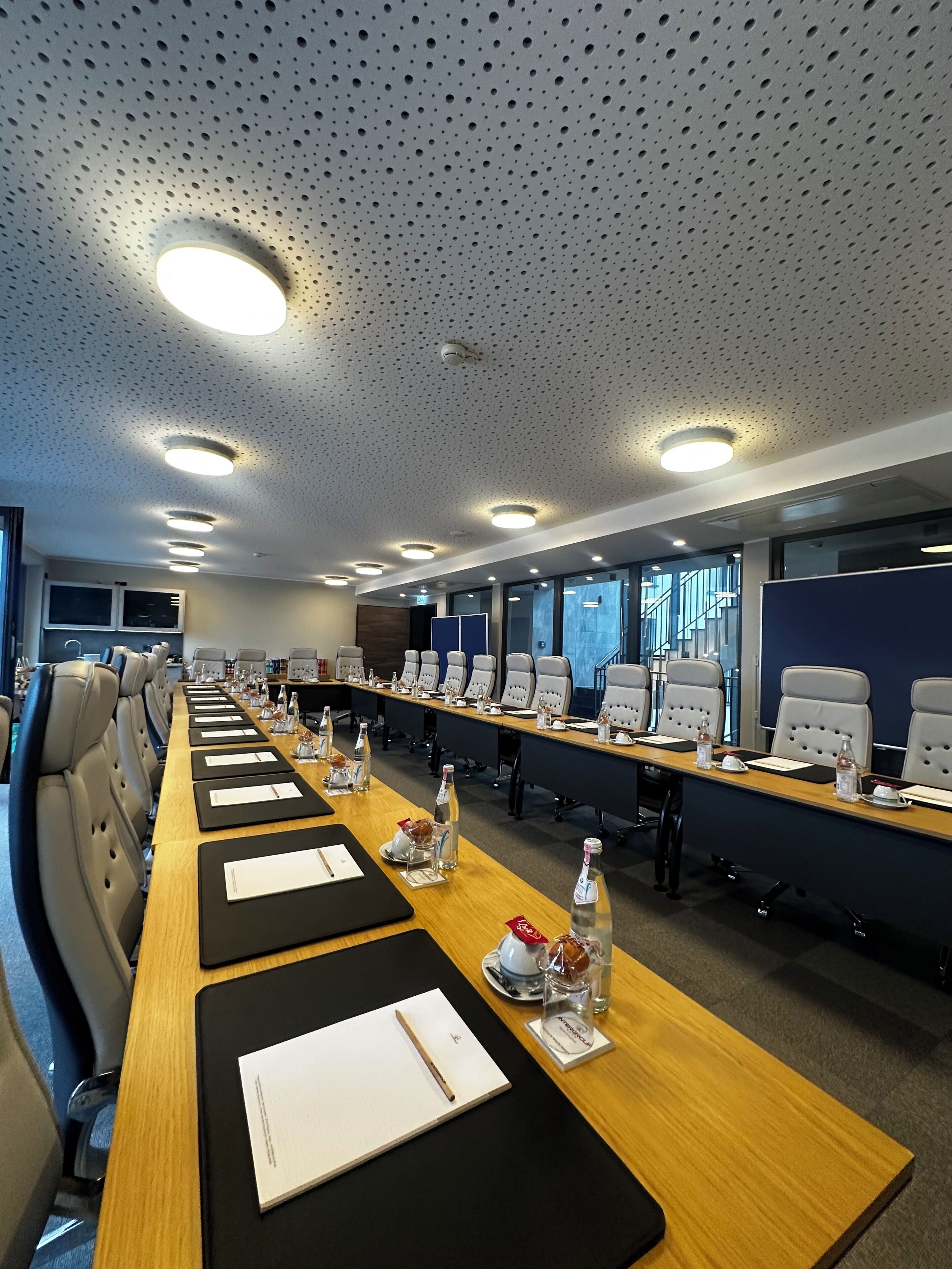 A conference room with a long table, chairs, and a ceiling with perforated panels and recessed lighting.