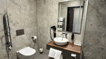 A modern bathroom with a marble wall, a white toilet, a wooden vanity with a large mirror, and a glass shower enclosure.
