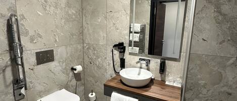 A modern bathroom with a marble wall, a white toilet, a wooden vanity with a large mirror, and a glass shower enclosure.