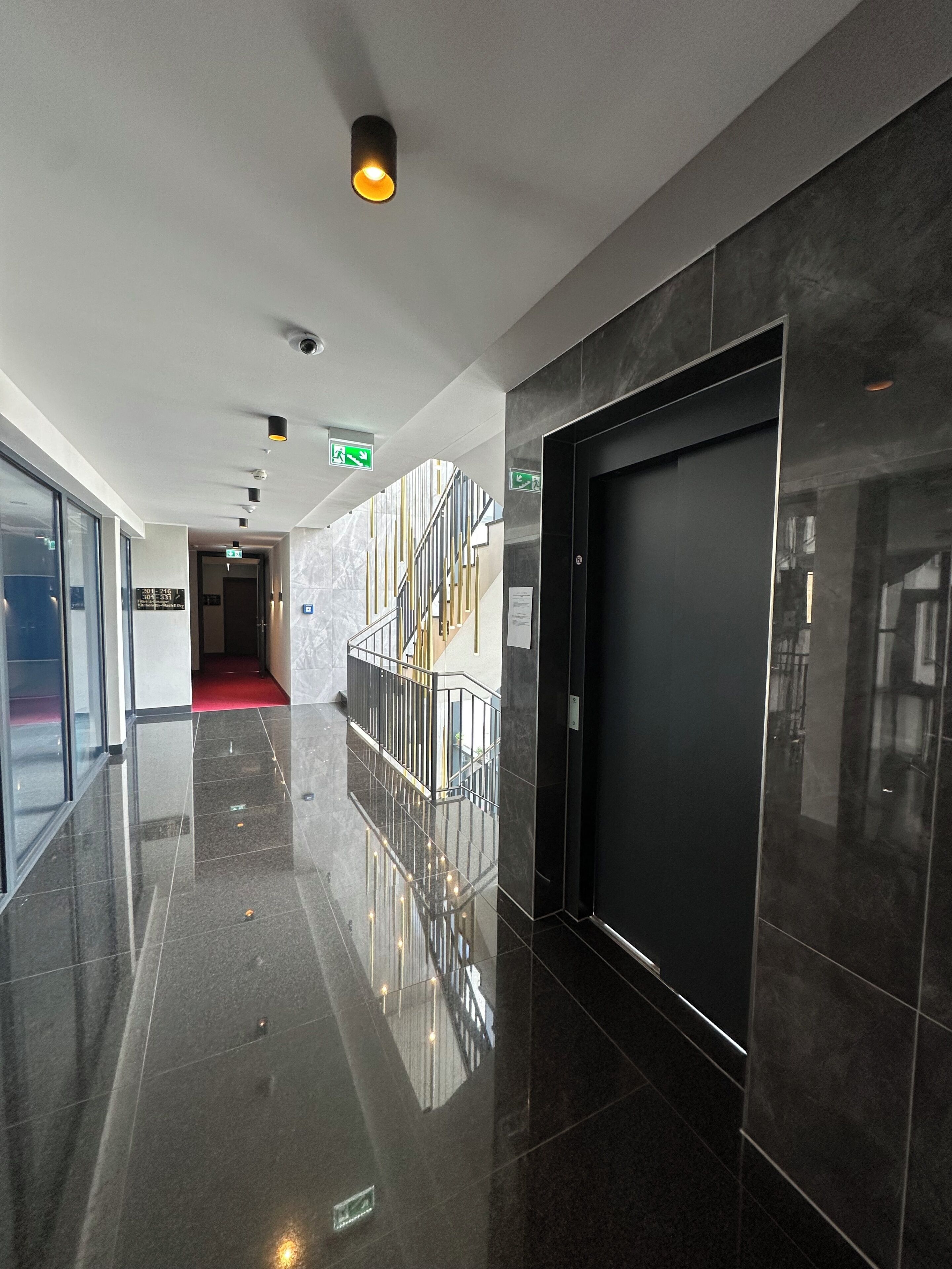 Un pasillo pulido con pisos reflectantes, una escalera y una puerta cerrada.