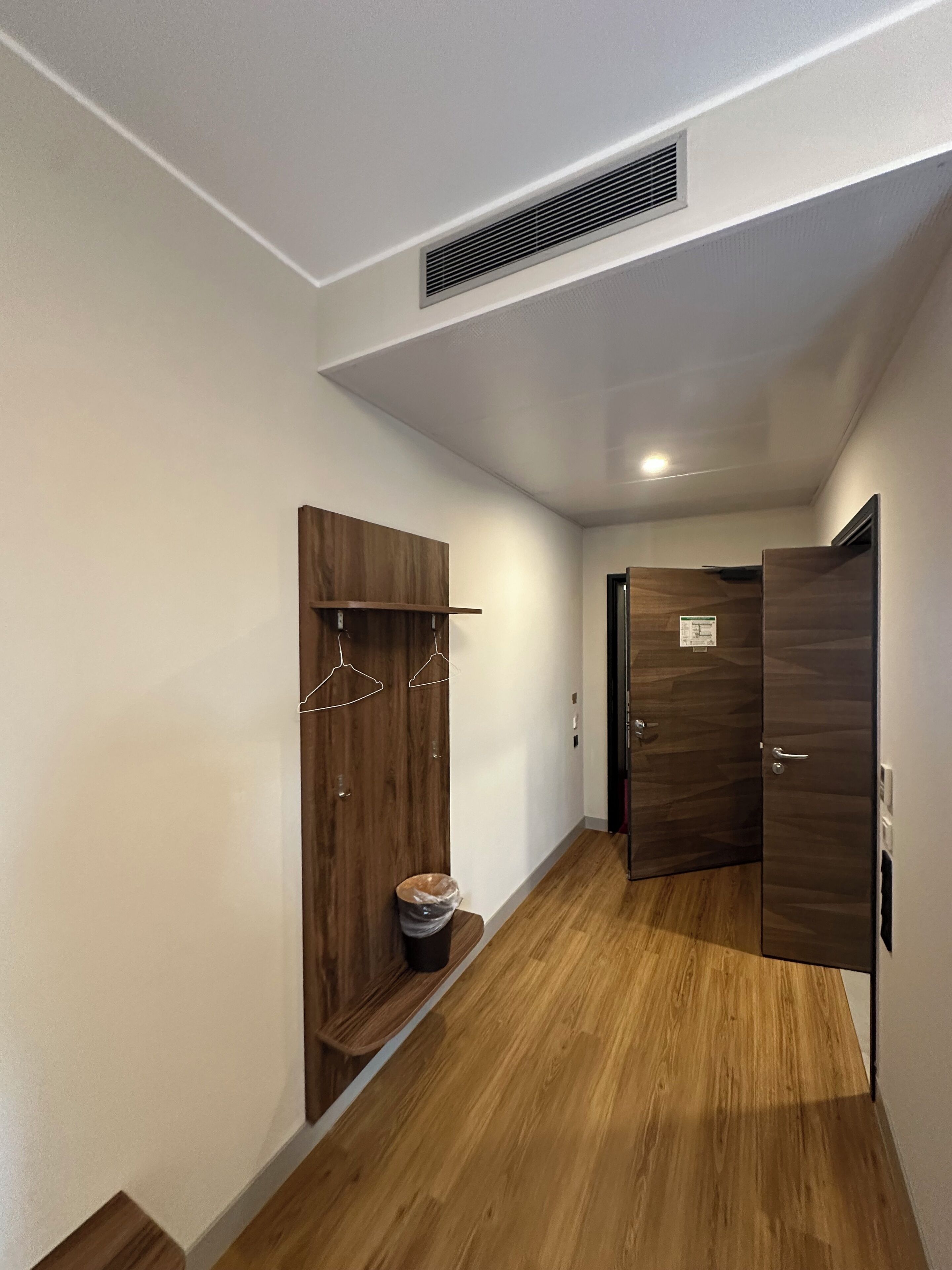 A hallway with wooden flooring, a coat rack, a trash bin, and a door with a sign.