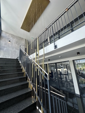 A modern interior with a staircase, metal railings, and a glass elevator. - Intergroup Business & Design Hotel Ingolstadt (Kosching)