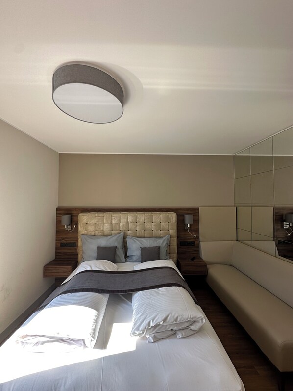 A modern hotel room with a large bed, a bench, a headboard with a textured design, and a large mirror on the wall.