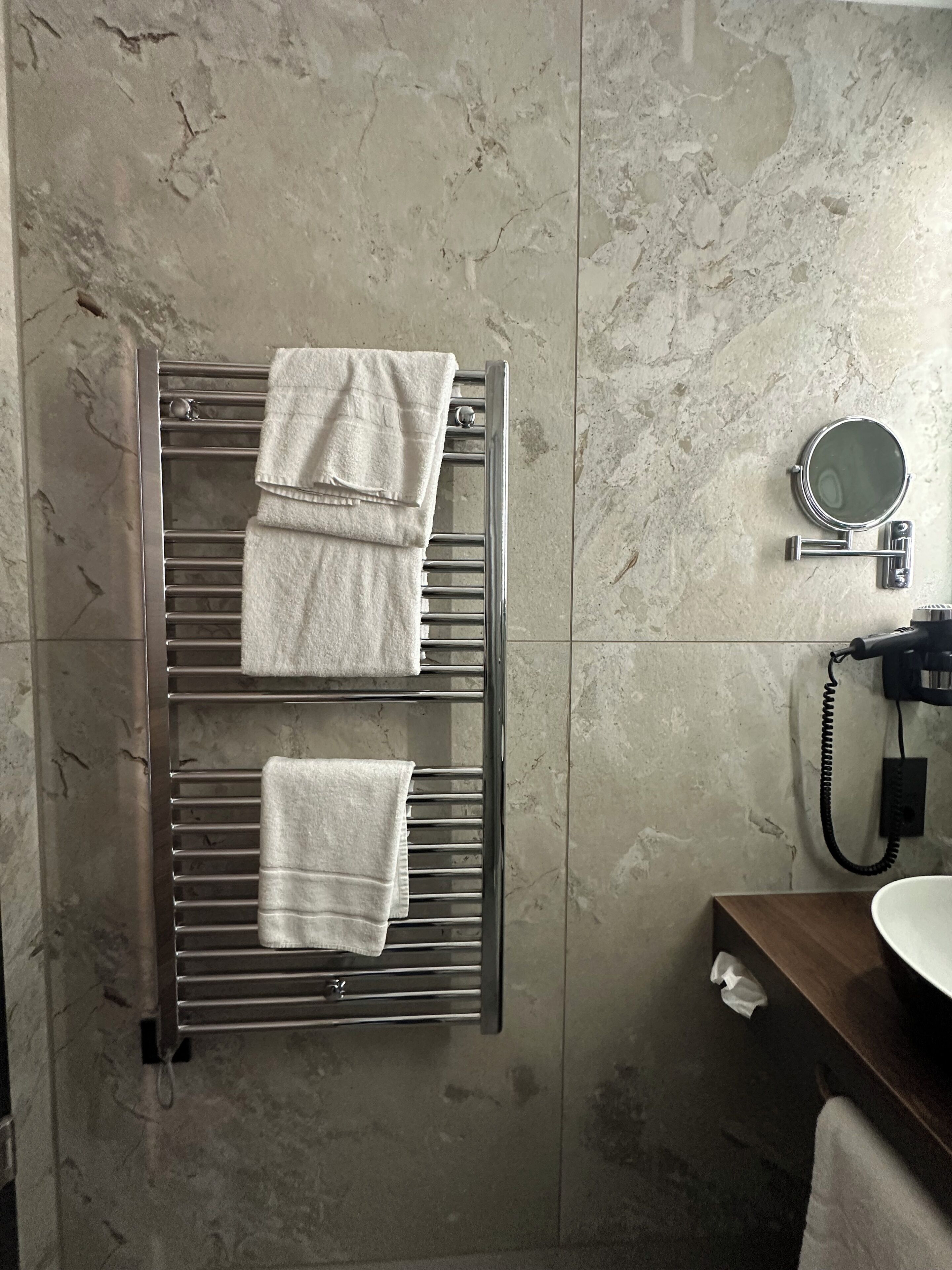 A bathroom with a towel rack holding two towels, a round mirror, and a telephone.