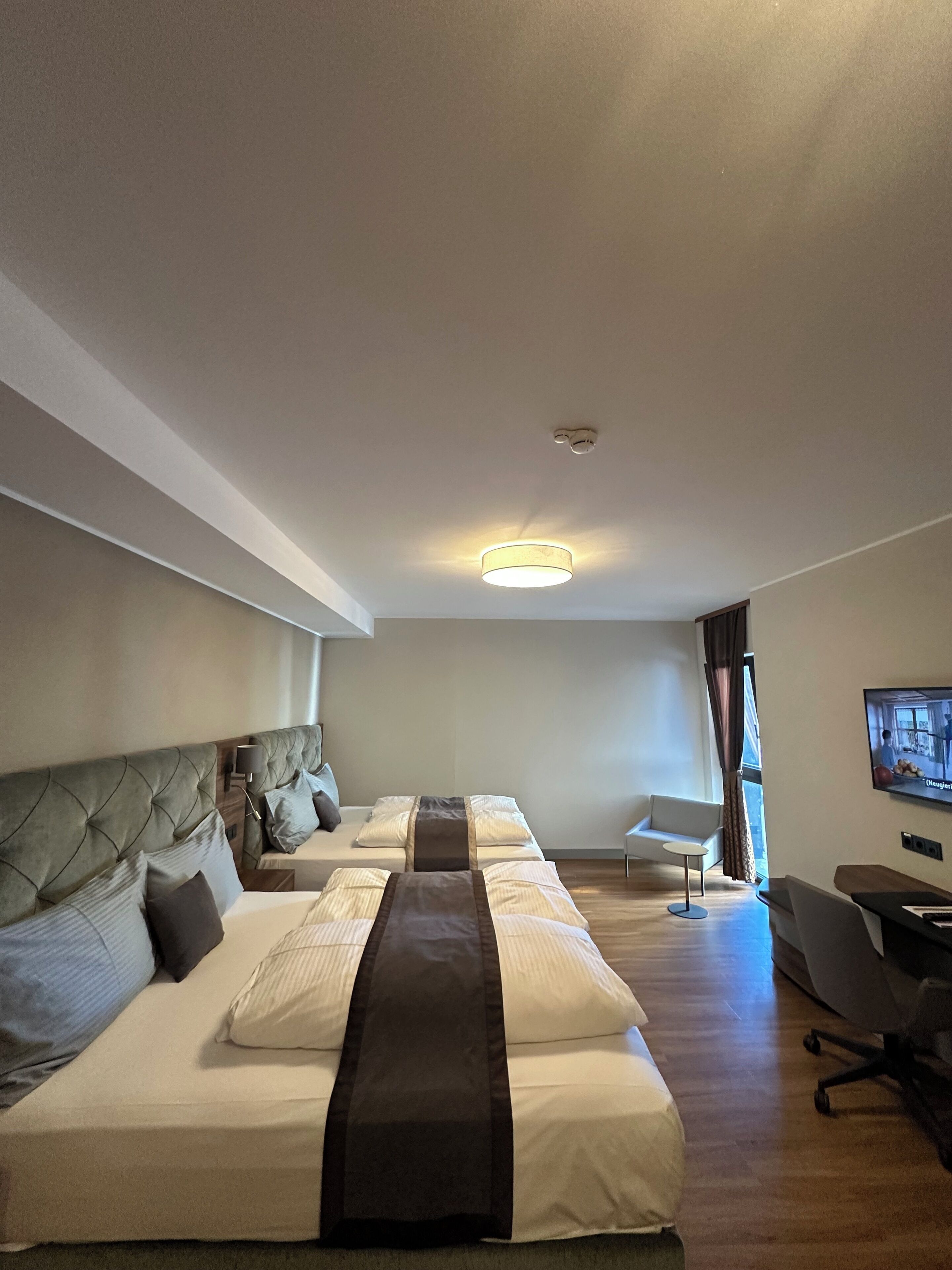 A hotel room with a large bed, a TV, a desk, and a window with curtains.