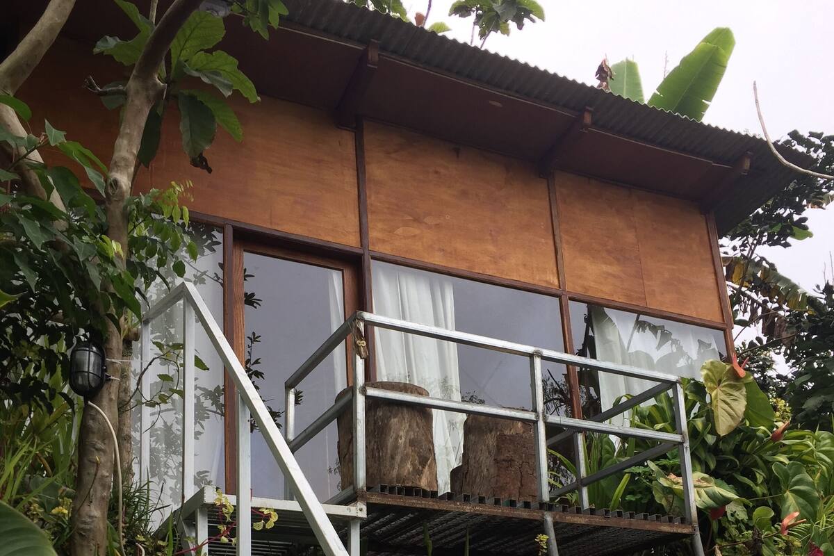 Um edifício de dois andares com varanda, cercado por vegetação exuberante.