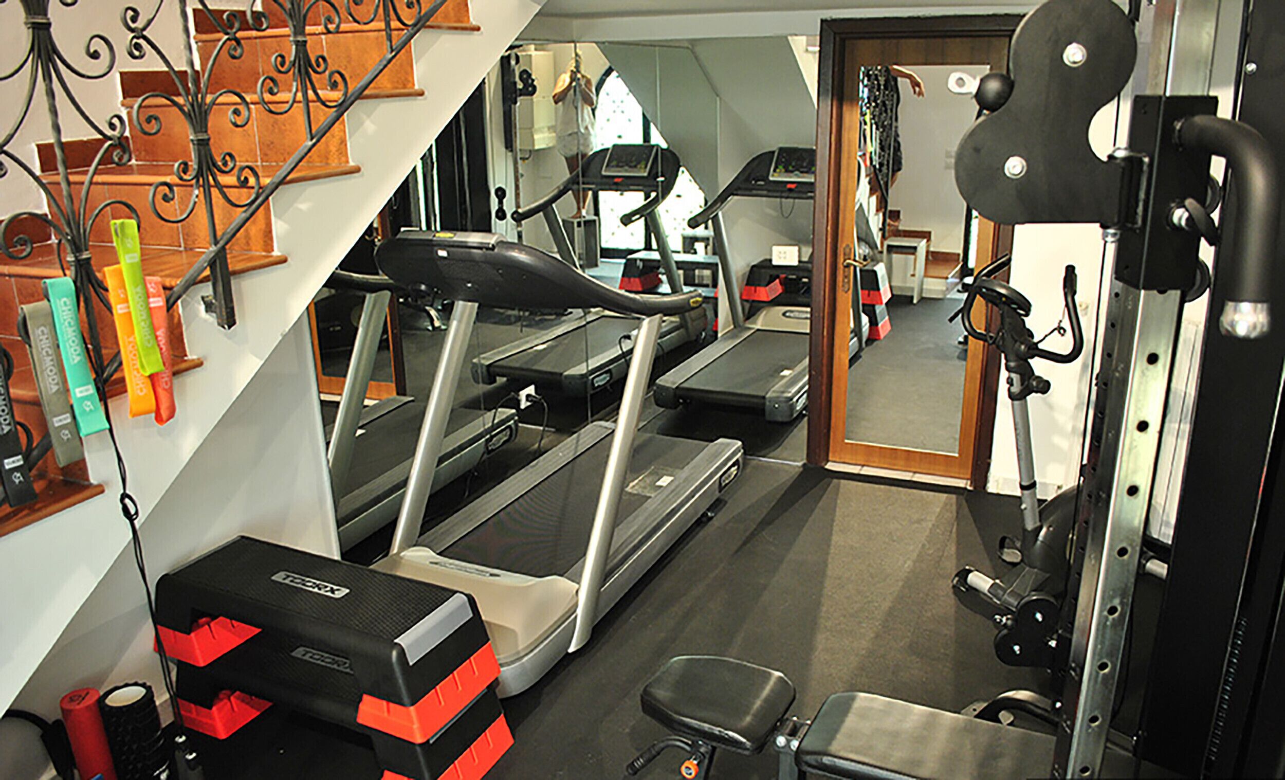 A home gym with treadmills, weightlifting equipment, and a staircase.