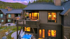 Un chalet à deux étages doté d’un bain à remous, d’un espace salon extérieur et d’une terrasse offrant une vue sur une région montagneuse.