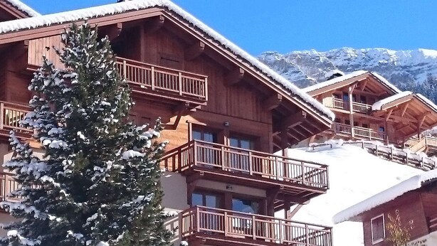 Een houten chalet met balkons, sneeuwbedekte daken en een berg op de achtergrond.