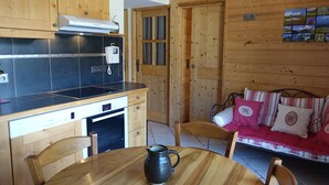 Een houten interieur met een keukenhoek, een eettafel met een mok en een bank met gestreepte kussens.