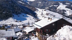 Een besneeuwde plaats met traditionele gebouwen, een kerk en bergen op de achtergrond.