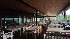En restaurang med träbord och stolar, stora fönster och ett högt tak.