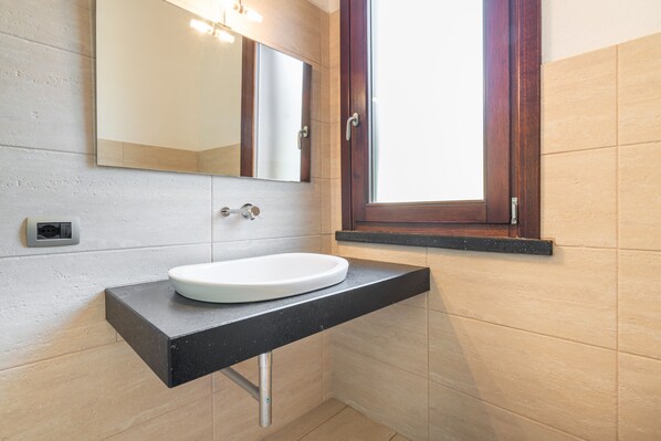 Un baño con un lavamanos blanco, un espejo y una ventana.
