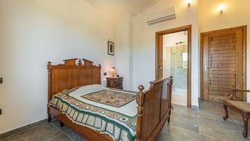 Un dormitorio con una cama de madera, una mesita de noche con una lámpara, un cuadro en la pared y una puerta de madera que da a un baño.