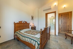 A bedroom with a wooden bed, a bedside table with a lamp, a framed picture on the wall, and a wooden door leading to a bathroom.