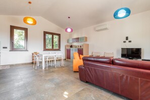 Una sala moderna con un sofá de cuero, un comedor con mesa y sillas blancas, y una cocina con armarios y un televisor.