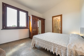 Un dormitorio con un ventanal grande, un armario, una cama con cubrecama blanco y una zona de ducha.