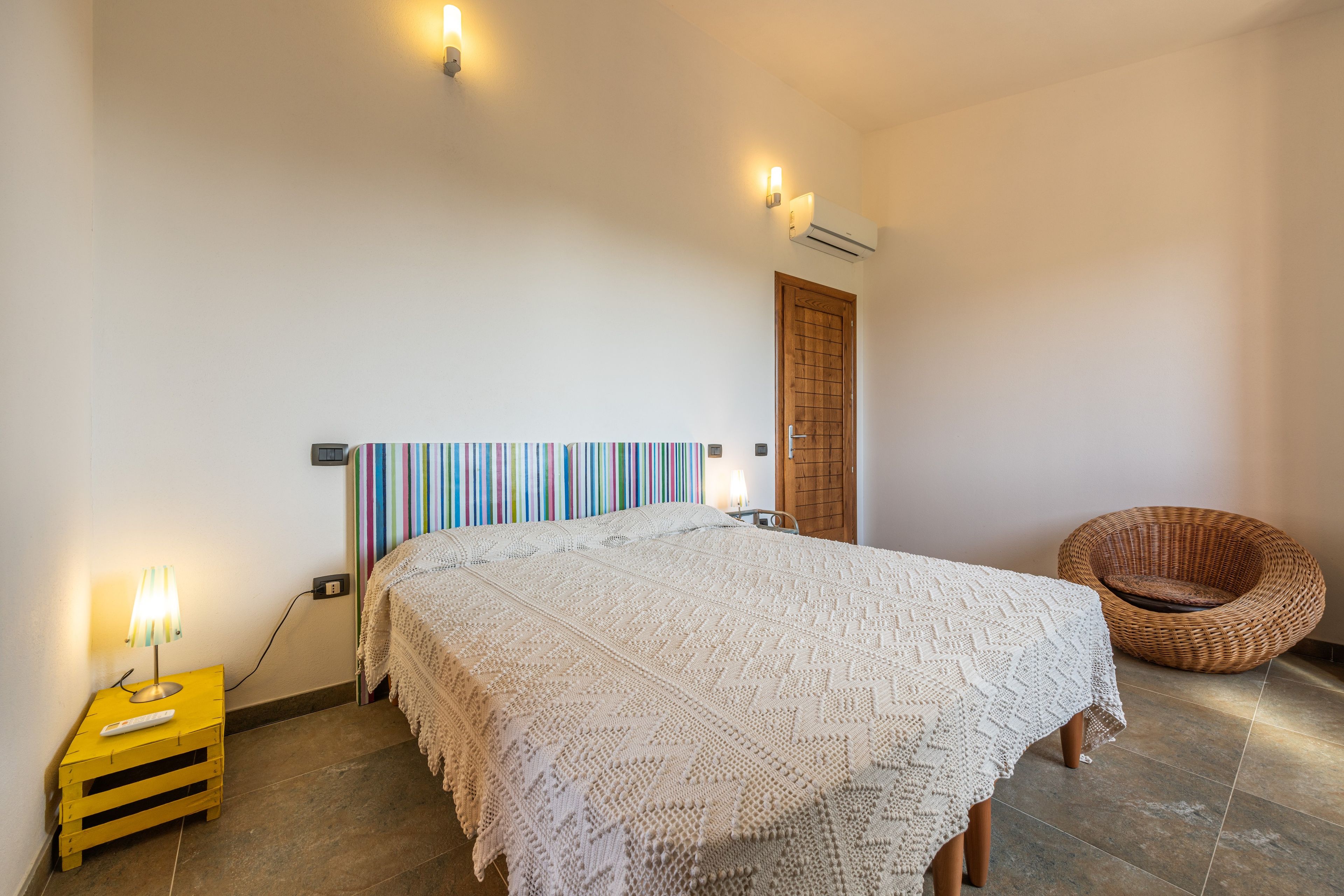 Un dormitorio con cama, lámpara de noche, una silla y aire acondicionado instalado en la pared.