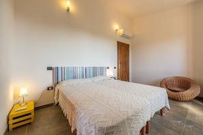 Un dormitorio con cama, lámpara de noche, una silla y aire acondicionado instalado en la pared.