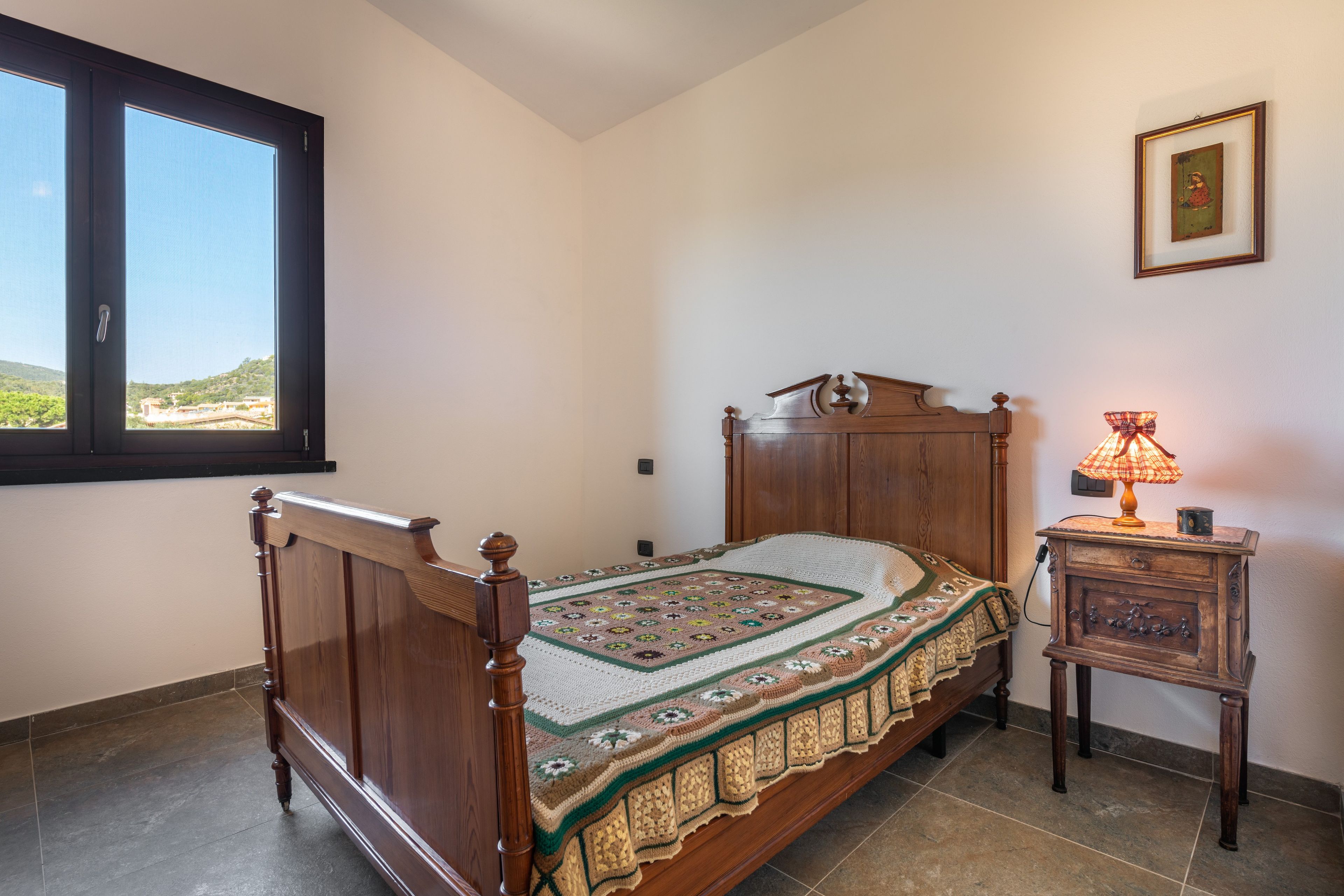 Une chambre à coucher avec un lit en bois, une table de chevet, une lampe et une fenêtre donnant sur un paysage verdoyant.