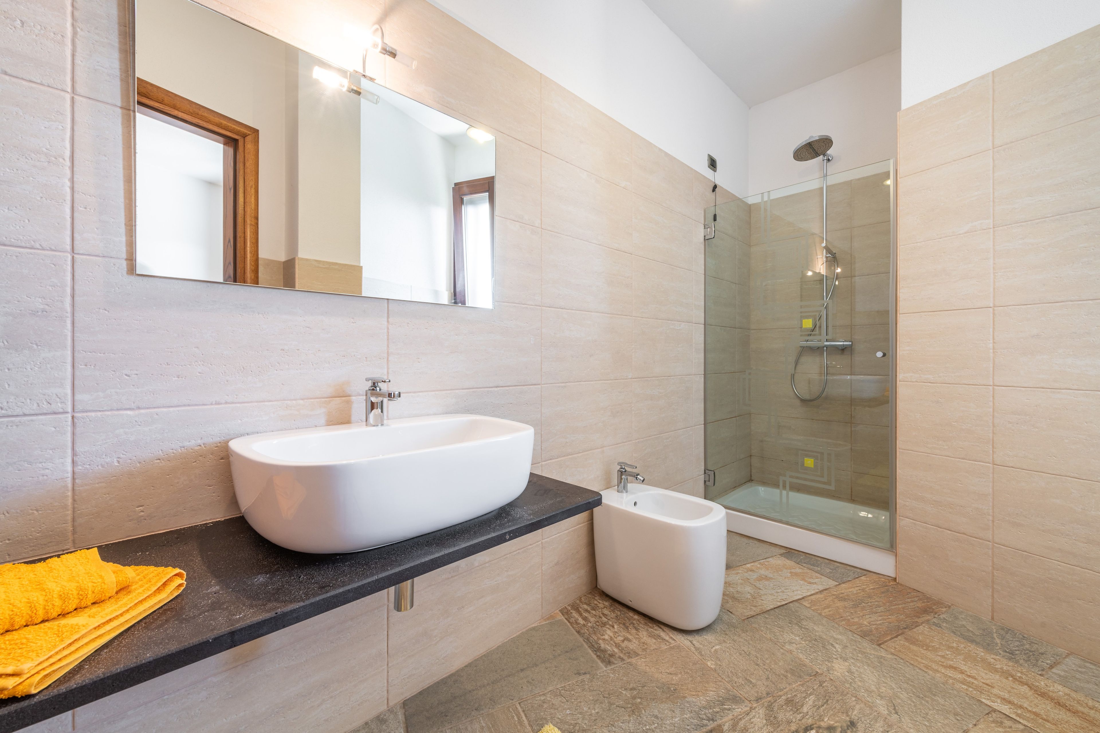 A bathroom with a large white sink, a mirror, and a glass-enclosed shower.