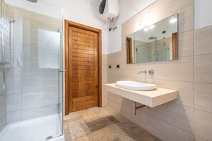Un baño moderno con cabina de ducha de vidrio, puerta de madera, lavamanos blanco y un espejo grande.