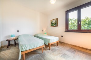 Ein Zimmer mit zwei Betten, einem kleinen Tisch, einem Gemälde und einem Fenster mit Blick auf Grünflächen.
