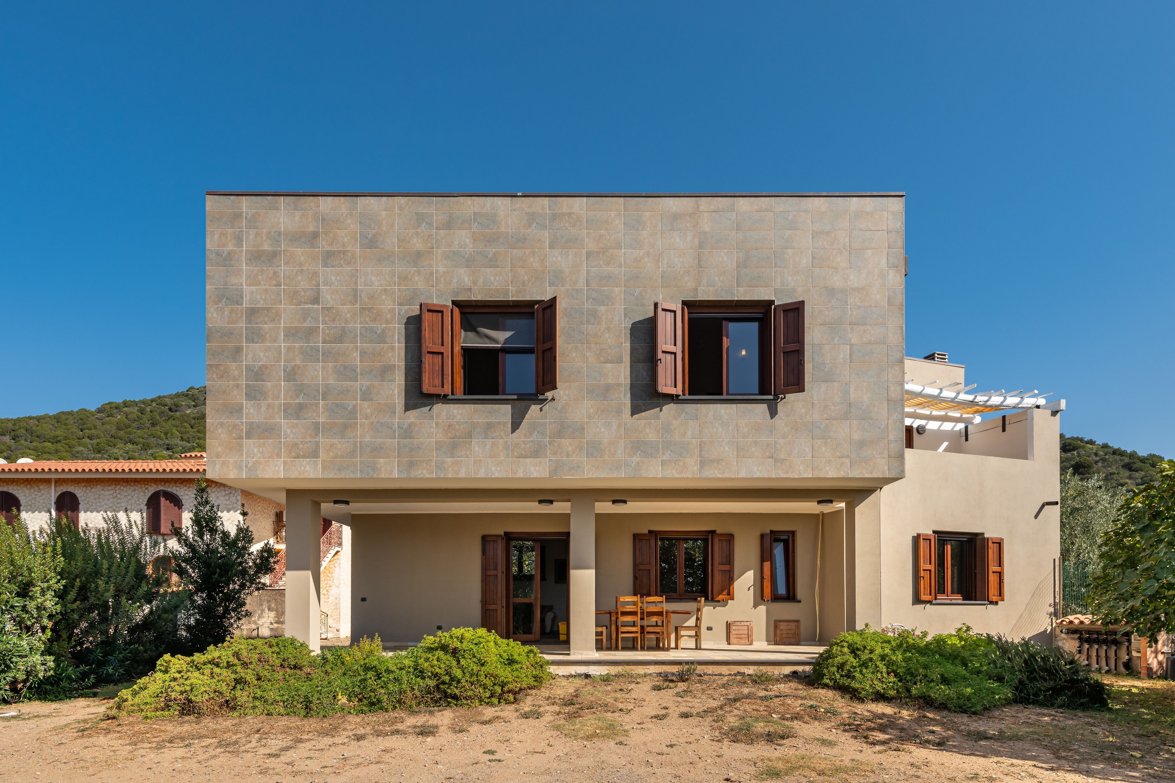 A two-story building with a flat roof, a balcony, and a covered outdoor seating area.