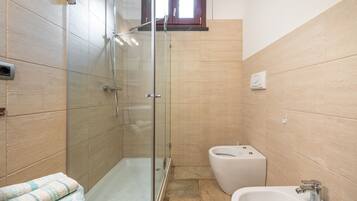 A bathroom with a glass-enclosed shower, a toilet, and a sink.
