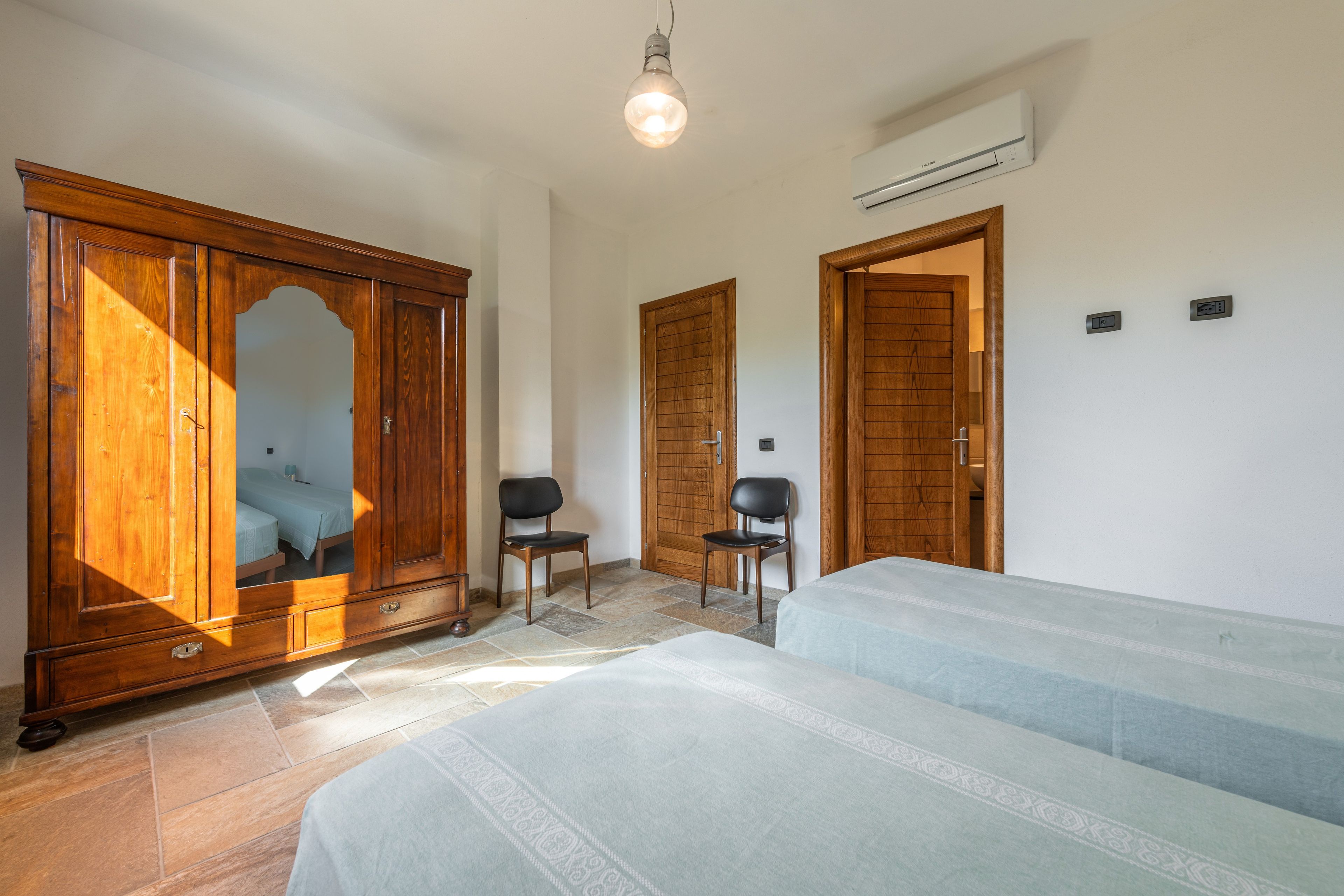 A bedroom with a bed, a wardrobe, a chair, and an air conditioning unit.