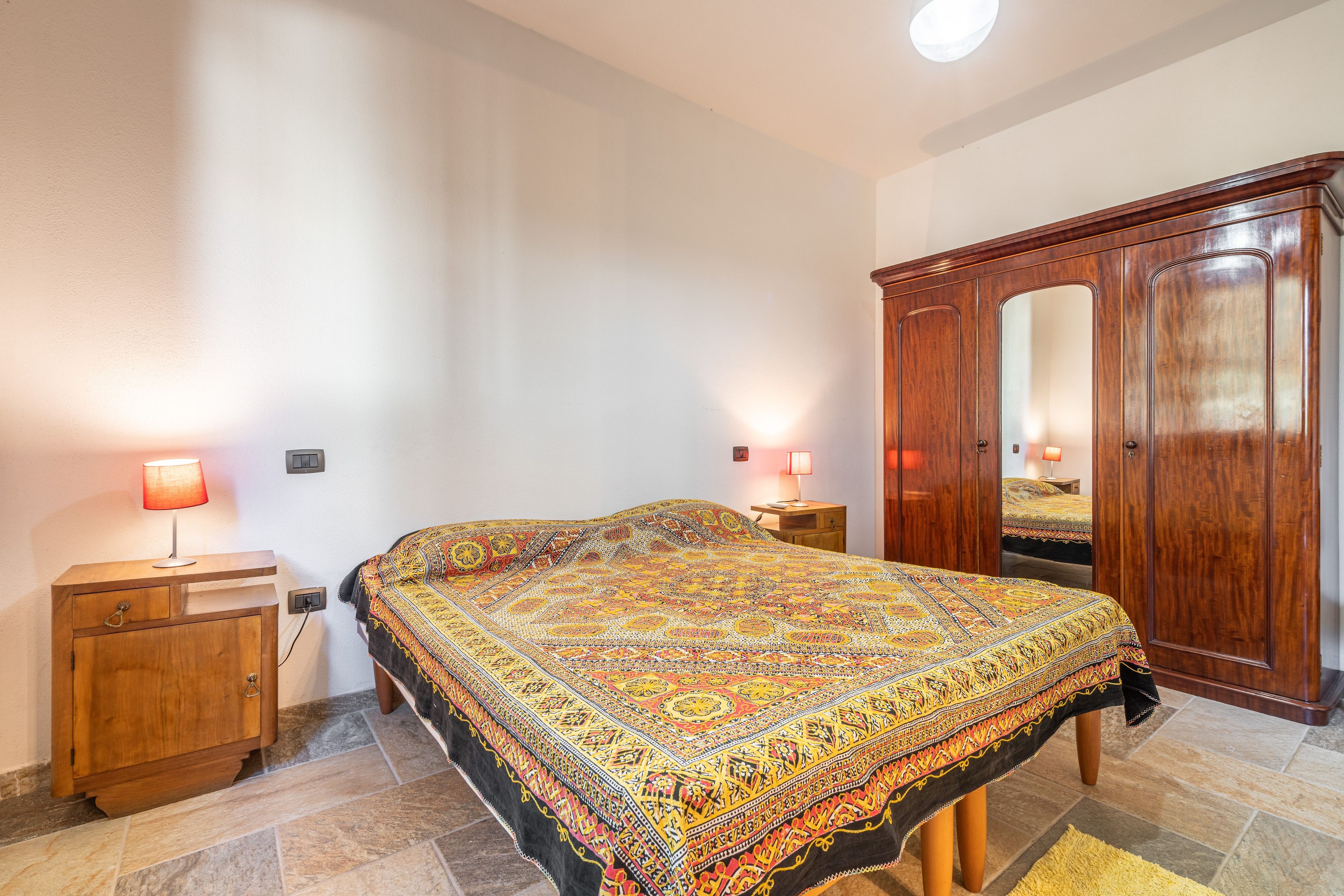 A bedroom with a large bed, a wooden wardrobe, a nightstand, and two bedside lamps.