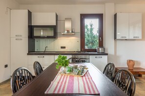 Une cuisine moderne avec des armoires blanches, une hotte de cuisinière en acier inoxydable et une fenêtre donnant sur un espace verdoyant.