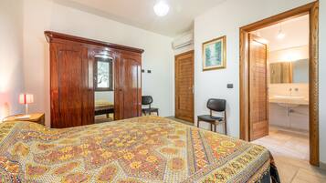 Un dormitorio con una cama grande, un armario, una silla, un escritorio y un baño con lavabo y espejo.