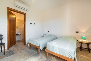 Een kleine, schone kamer met twee eenpersoonsbedden, een houten stoel, een klein tafeltje met een lamp en een airconditioner aan de muur.