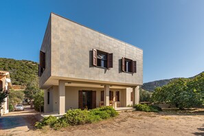 Ein modernes, zweistöckiges Haus mit Flachdach, großen Fenstern mit Fensterläden und einer überdachten Veranda.