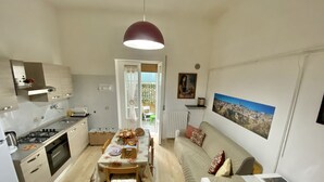 A compact kitchen with a dining table, chairs, and a sofa. There is a radiator, a painting on the wall, and a window with curtains. - CasaBattista10 Comfort and Relax (Matera)