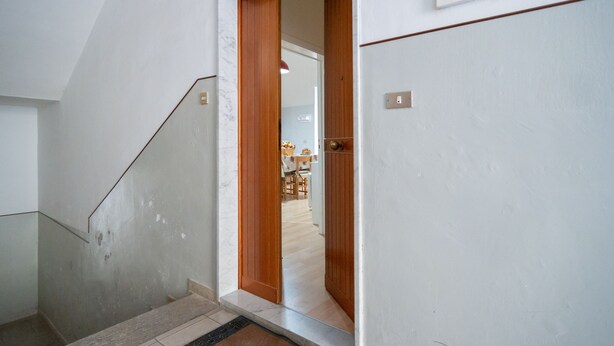 A staircase leading to a room with a wooden door and a visible kitchen area in the background. - CasaBattista10 Comfort and Relax (Matera)