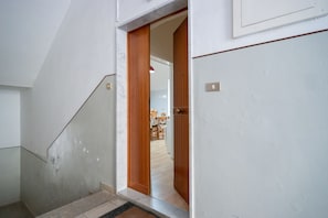 Una escalera conduce a una habitación con una puerta de madera y una cocina visible al fondo.