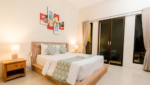 Um quarto com cama de madeira, duas mesas de cabeceira com luminárias, uma janela grande com cortinas e uma porta de vidro deslizante que dá para uma varanda.