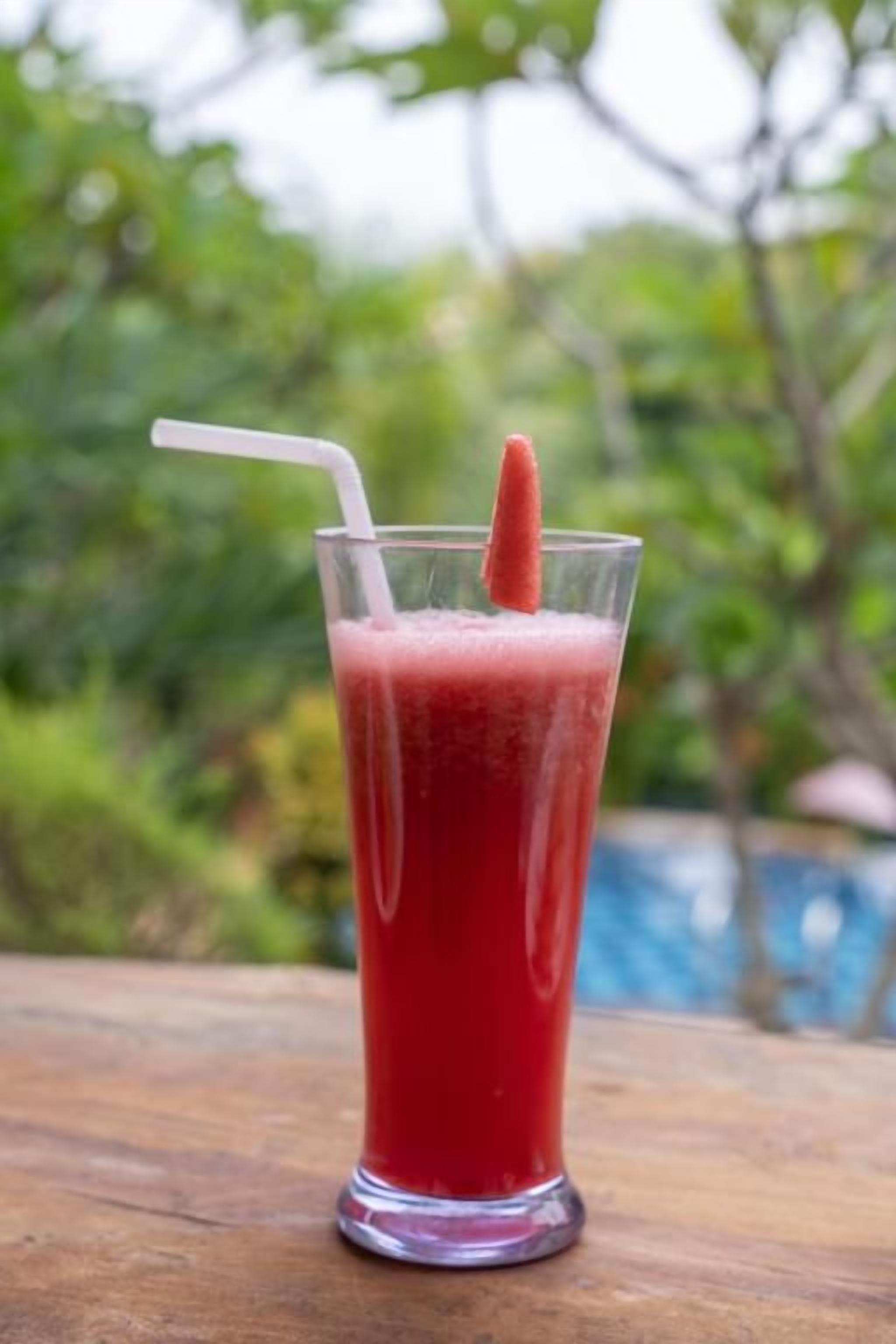 Un verre contenant une boisson rouge, avec une paille et une tranche de fruit, posé sur une surface en bois.
