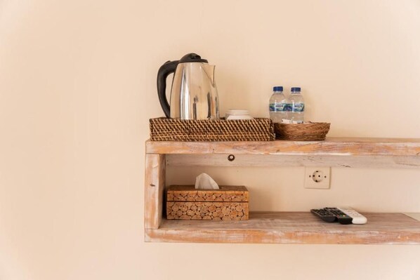 A wooden shelf with a kettle, water bottles, a tissue box, and a remote control.